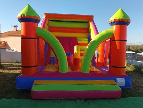 Colorful inflatable bounce house with red towers, green curved slides, and blue base in outdoor setting
