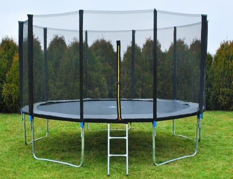 Large round trampoline with black safety net and metal frame in grassy yard with trees in background