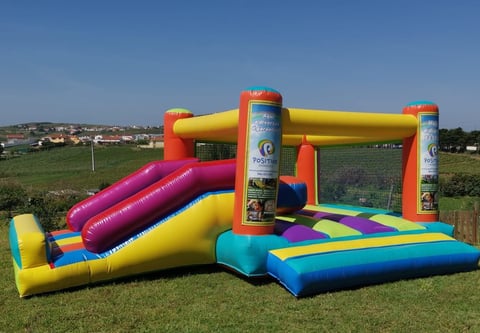 Large inflatable bounce house with colorful sections including slide and obstacle course in grassy outdoor field
