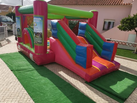 Colorful inflatable bounce house with slide and climbing wall in pink, green, and blue set up on artificial grass in a residential driveway