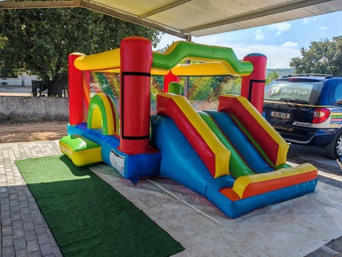 Colorful inflatable bounce house with slide on outdoor patio surrounded by trees and vehicles
