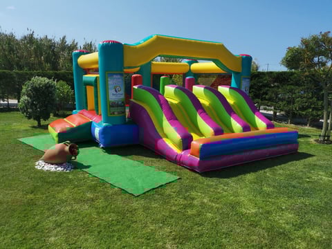 Colorful inflatable bounce house and slide on green grass with trees in background under clear sky