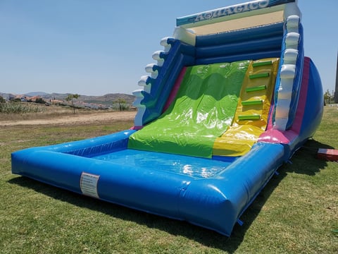 Colorful inflatable water slide bounce house with blue base and green slide on outdoor grass field