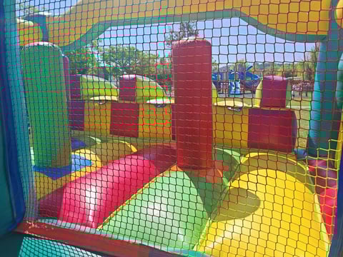 Colorful indoor play structure with inflatable obstacles and slides enclosed by mesh netting in a childrens play area