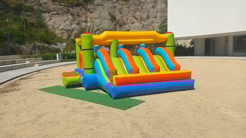 Colorful inflatable bounce house with slide on sandy ground in outdoor recreational area near rocky cliff