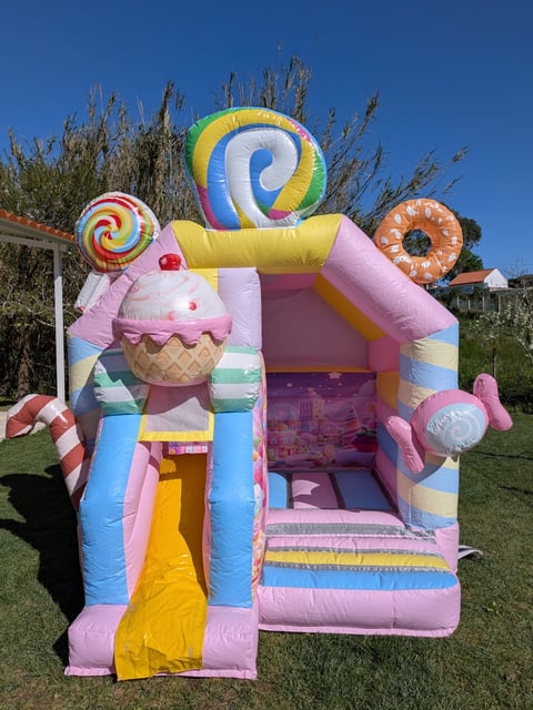 Colorful inflatable bounce house with candy theme featuring ice cream, lollipop, and donut designs in a backyard setting