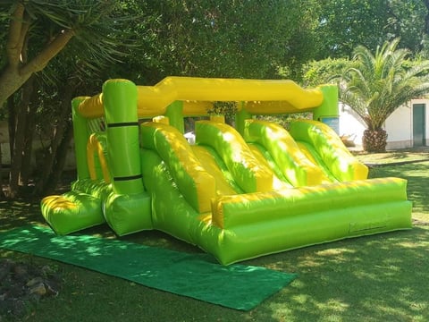 Bright green and yellow inflatable bounce house with slide in a sunny backyard with trees
