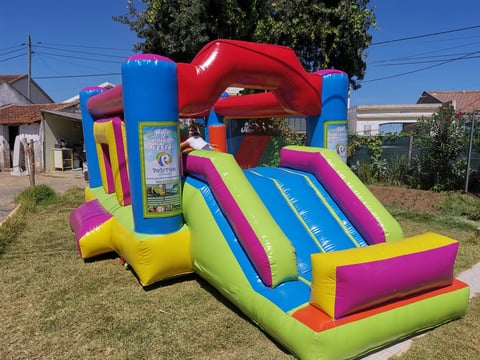 Colorful inflatable bounce house and slide set up on grass in a residential yard, featuring red, blue, yellow, and pink panels with a slide attachment.