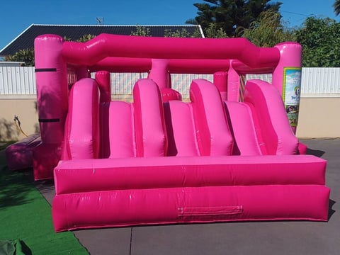 Bright pink inflatable bounce house with multiple slide lanes and climbing features in outdoor setting