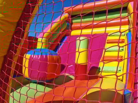 Colorful inflatable bounce house with bright pink, yellow, blue, and green netting and structural elements