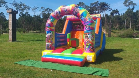 Colorful inflatable bounce house with arch roof on grass field with trees in background on sunny day