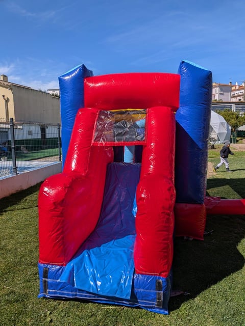 Red and blue inflatable bounce house with slide on grassy outdoor area