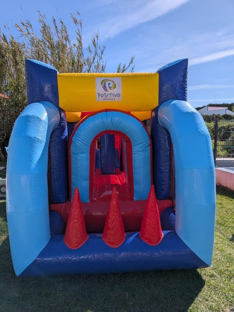 Colorful inflatable bounce house with blue sides, yellow top, and red obstacles on grassy outdoor area